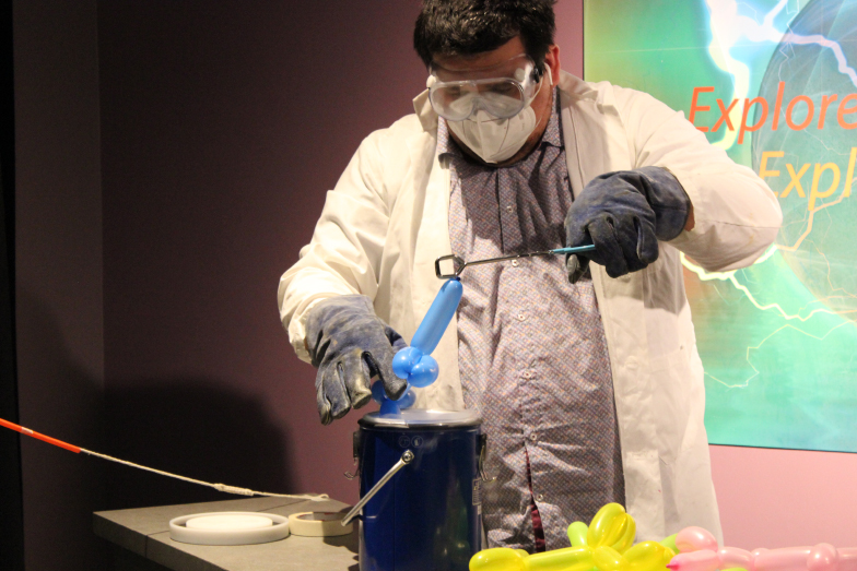 A person in a lab coat is dipping a balloon animal into some dry ice.
