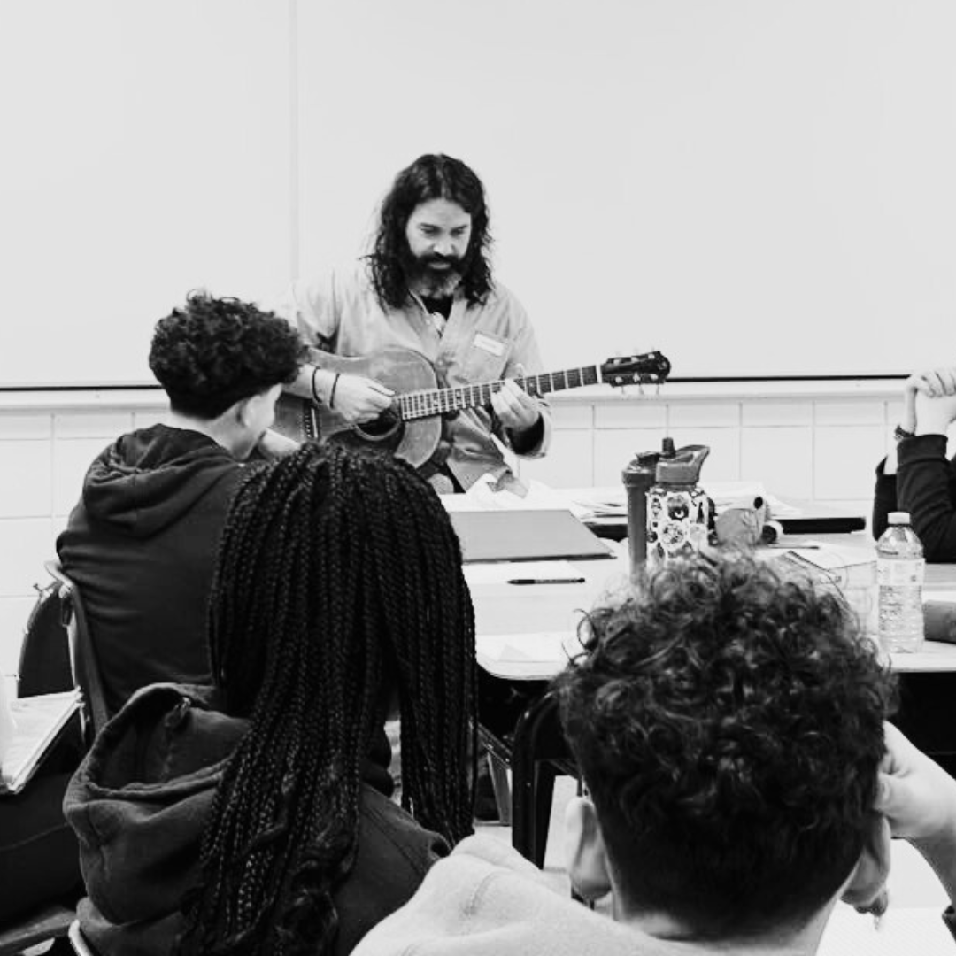 A teacher plays guitar in front of his students